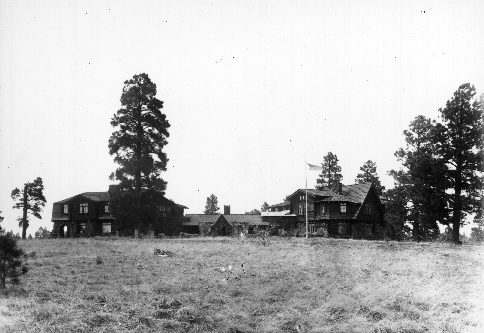 A brick mansion sits on a rise in the field, surrounded by a few trees.