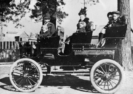 Paul Babbitt Senior, his wife and four children pose in an early topless automobile with three rows of seats.