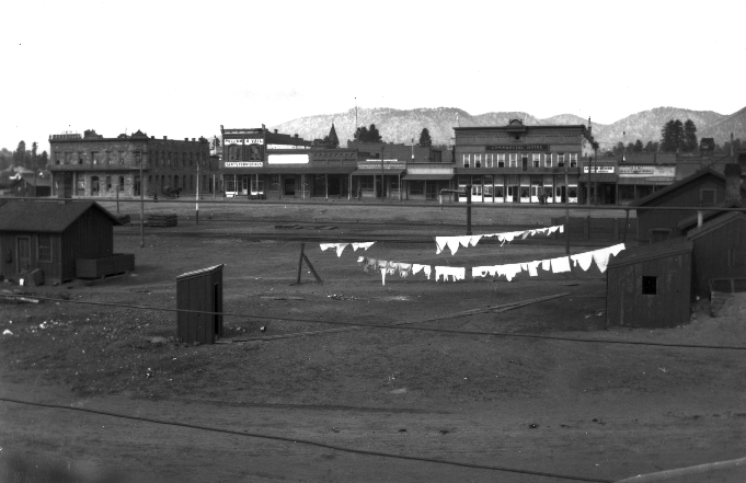 A north-facing view of Santa Fe Boulevard (now Route 66) as seen from Phoenix Avenue between San Francisco Street and South Agassiz Street. In the foreground are shacks, a laundry line drying and an outhouse.