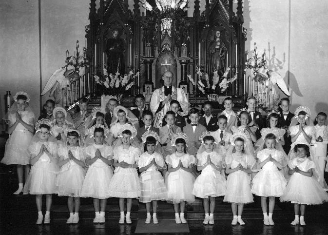 A group of thirty elementary-school age girls and boys pose in front of the altar,