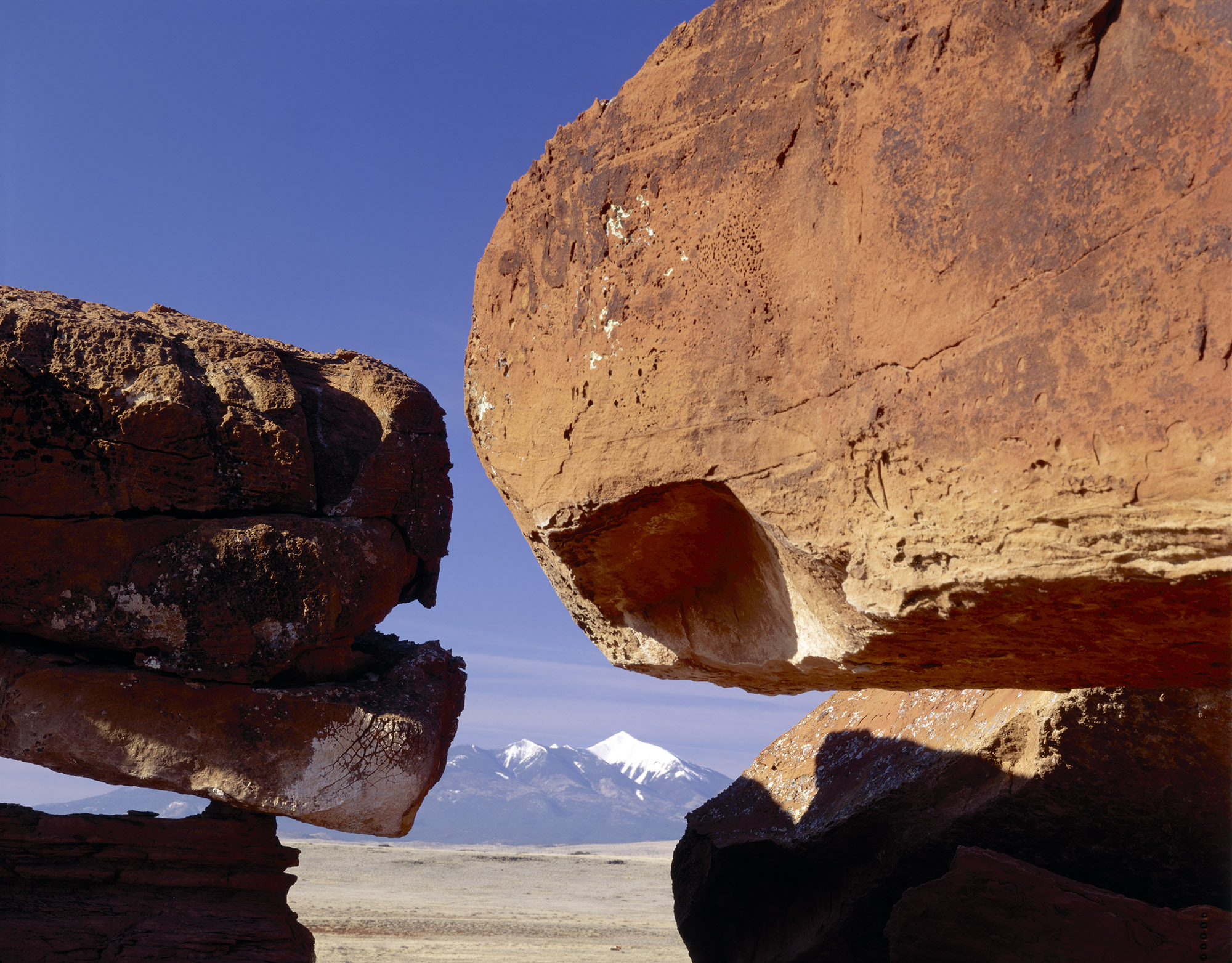 Two sandstone boulders, with the San Francisco Peaks visible in the far distance